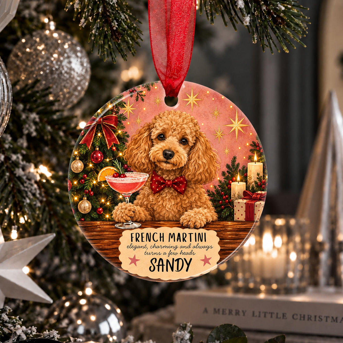 A round Christmas ornament featuring a fluffy golden-brown dog sitting at a table with a cocktail glass, surrounded by holiday decorations. The ornament has a red ribbon hanging from the top and a printed message that reads 'French Martini elegant, charming and always wears a few beads SANDY'.