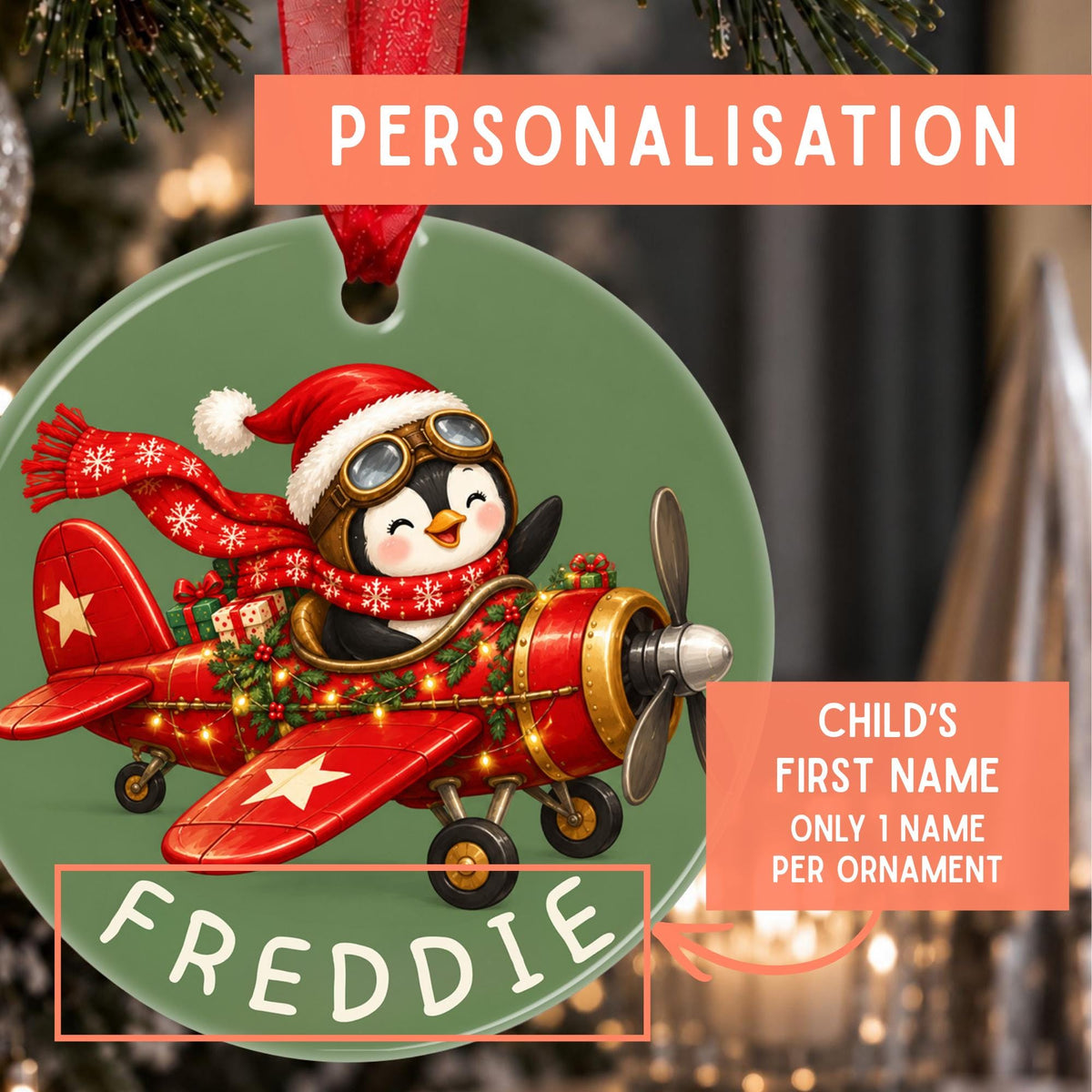 A green christmas ornament hanging on a xmas tree with a penguin in a plane with the personalised name on it. There is a text stating Child's First Name Only 1 Name Per Ornament.