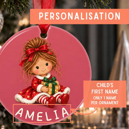 Personalized Christmas ornament featuring a cartoon girl in a red dress holding a gift, with the name 'AMELIA' and a red ribbon loop. The image includes promotional text overlays explaining the personalization option.