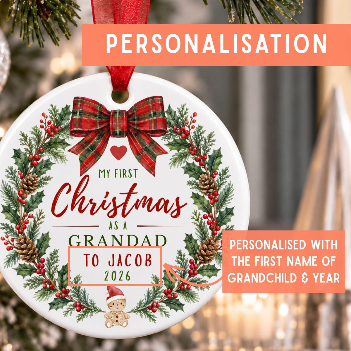 Personalized round Christmas ornament with a red ribbon hanger, featuring a festive wreath design with holly, pinecones, red berries, and a red plaid bow. The ornament is printed with the text 'MY FIRST Christmas AS A GRANDAD TO JACOB 2026' and includes promotional text overlays highlighting personalization.