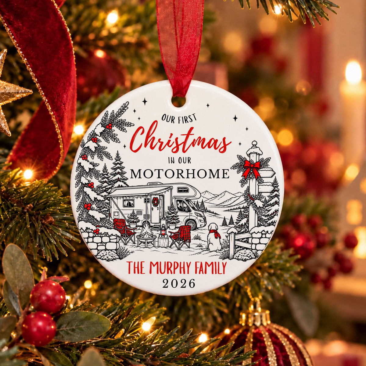 A personalized round Christmas ornament hanging from a red ribbon on a decorated Christmas tree. The white ornament features a black line art illustration of a motorhome, campfire, mountains, and trees, with red script text reading 'Our First Christmas in our MOTORHOME' and 'THE MURPHY FAMILY 2026'.