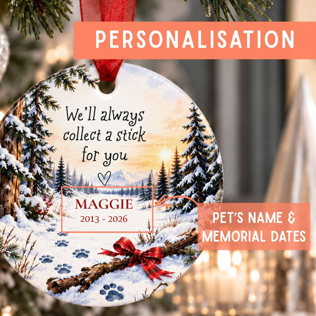 Personalized round Christmas ornament hanging on a tree, featuring a winter forest scene with snow, pine trees, mountains, and a red ribbon. The ornament includes printed memorial text reading 'We'll always collect a stick for you' and 'Maggie 2013 - 2026', with orange promotional labels around it explaining personalization.