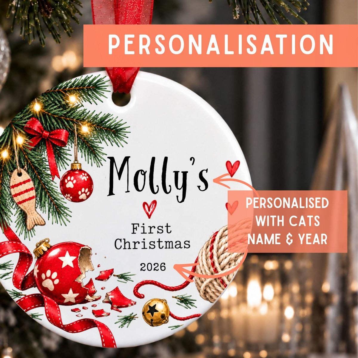 Personalized round Christmas ornament hanging on a tree, with printed text reading 'Molly's First Christmas 2026' and decorative red ribbon, ornaments, pine branches, and a paw print. Coral overlay banners say 'PERSONALISATION' and 'PERSONALISED WITH CATS NAME & YEAR'.