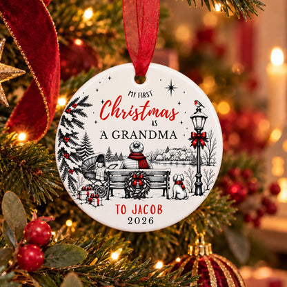 A personalized round Christmas ornament hanging on a decorated tree. The white ornament features a black line art illustration of a woman sitting on a bench with a dog, alongside red text reading 'My First Christmas As A Grandma To Jacob 2026' and red ribbon accents.