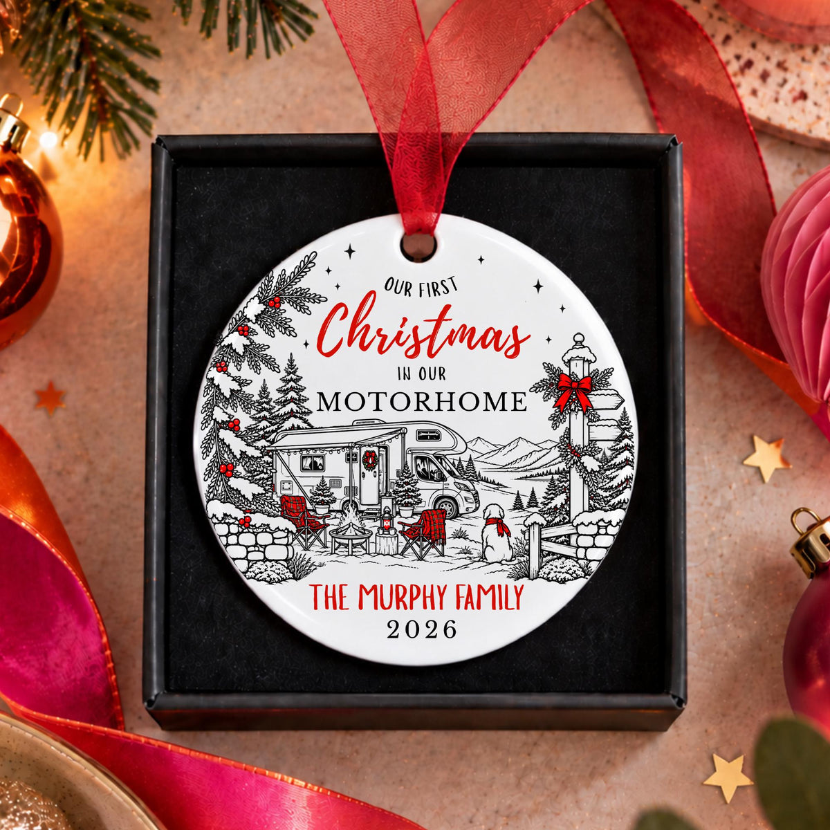 A personalized round Christmas ornament displayed in a black gift box, featuring a winter camping scene with red ribbon and red text reading 'Our First Christmas in our Motorhome The Murphy Family 2026'.