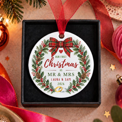 A personalized round Christmas ornament displayed inside a black gift box, featuring a festive wreath design with a red plaid bow and custom text reading 'Our First Christmas as Mr. & Mrs.