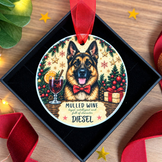A personalized Christmas ornament in a black square gift box, featuring a German Shepherd dog wearing a red bow tie, surrounded by festive holiday illustrations and the text 'MULLED WINE' and 'Diesel'.