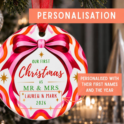 Personalized Christmas ornament featuring a colorful candy-striped border, a pink bow illustration, and custom text reading 'Our First Christmas as Mr & Mrs Lauren & Mark 2026' on a blurred holiday tree background.