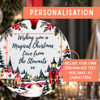 Personalized round Christmas ornament mockup hanging on a decorated tree, with a red ribbon, festive village illustration, and text areas showing customization options.